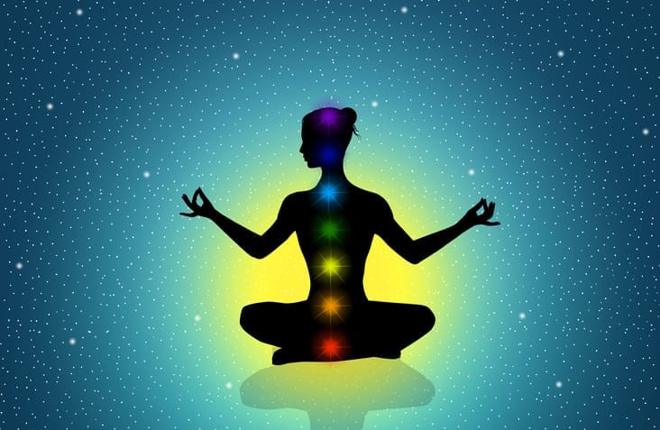 Silhouette meditating with chakras in cosmic background.