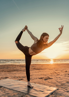 Yoga practitioner in dancer pose on a mat at sunset by the sea